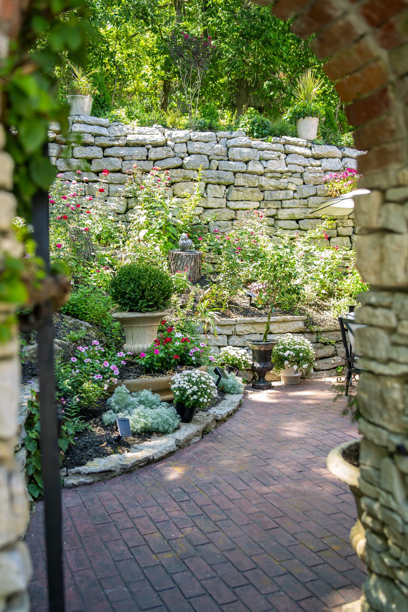 Brick path curving through the terraced rose garden below a stone wall
