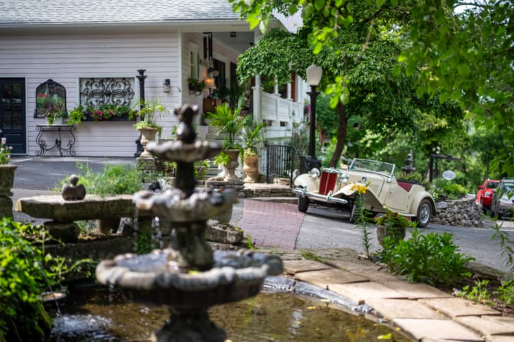 Tiered stone fountain in front of the inn, with a vintage roadster parked on the drive